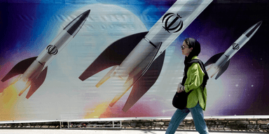 En kvinna går förbi en banderoll som visar hur missiler avfyras i norra Teheran, Iran, den 19 april 2024.