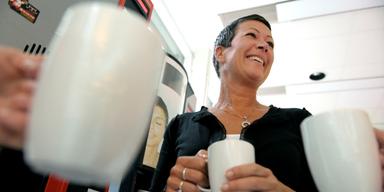 En kvinna dricker kaffe tillsammans med kollegor under en fikapaus.