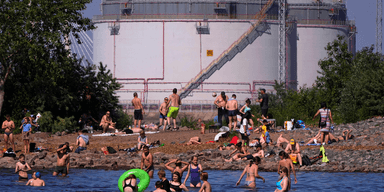 Människor simmar i Östersjön, intill en lagringstank för olja nära Sankt Petersburg i Ryssland.