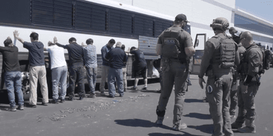 Denna bild från en video från U.S. Immigration and Customs Enforcement via DVIDS visar anställda på en fabrik som väntar på att få sina ben bojade vid Hyundai Motor Groups elbilsfabrik. (Foto: Corey Bullard/AP/TT)