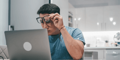 Ung man sitter framför laptop och ser bekymrad ut när han söker jobb online, symboliserar stigande arbetslöshet i Sverige.