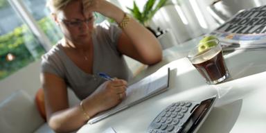 Kvinna använder miniräknare och betalar räkningar vid köksbordet, går igenom sin privatekonomi inför beslut om privatlån.