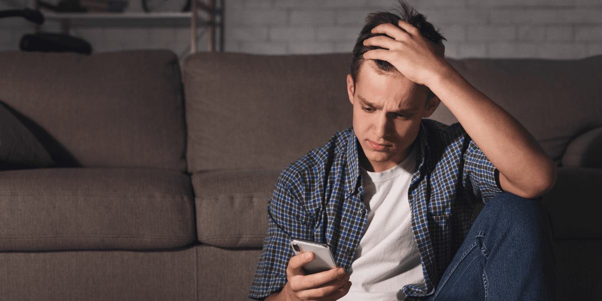 Ung man ser bekymrad ut medan han tittar på mobilen, en symbol för investeringsångest och FOMO.