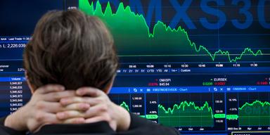 Person tittar på en datorskärm som visar kursfall och grafer för OMXSPI och andra börsindex under 2025.