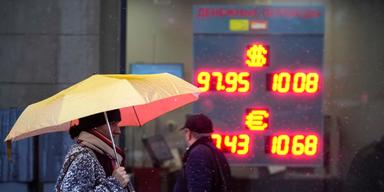 En kvinna med paraply passerar växlingsskylt i Moskva. Inflationen faller, men hushållen påverkas fortfarande av höga räntor och svag rubel.