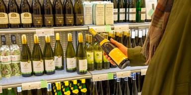 Person håller i en vinflaska framför en butikshylla med alkohol, bland annat rieslingviner.