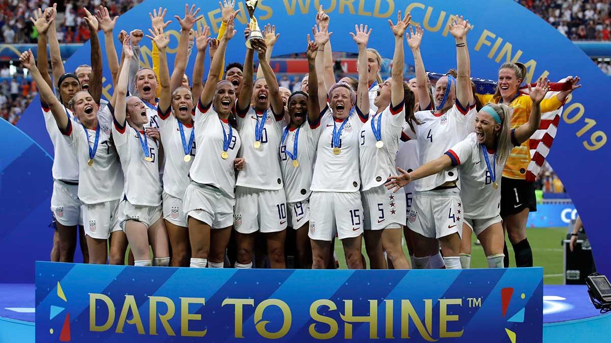 De amerikanska fotbollsdamerna jublar över VM-guldet i fotboll 2019, och Sophie Hedberg reflekterar över texten på banderollen vid deras fötter: "Dare to shine" (Våga lysa). (Foto: TT)
