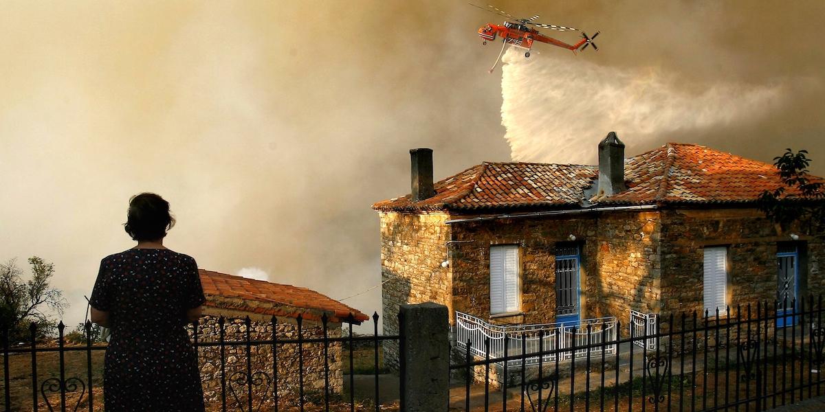 En kvinna tittar på sitt hus som hotas av branden, Europas extremväder har nu gjort att skogsbränder härjar nära Greklands huvudstad Aten