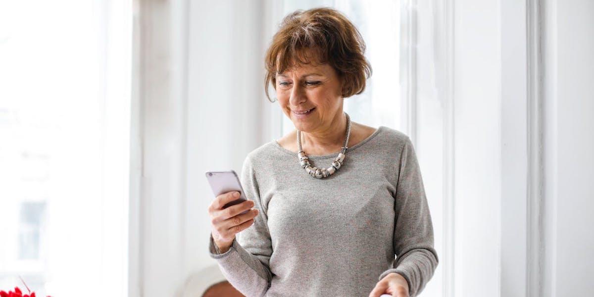En kvinna läser i sin mobil. En regel säger att de med garantipension får mindre om de tar ut sin allmänna pension innan 66.