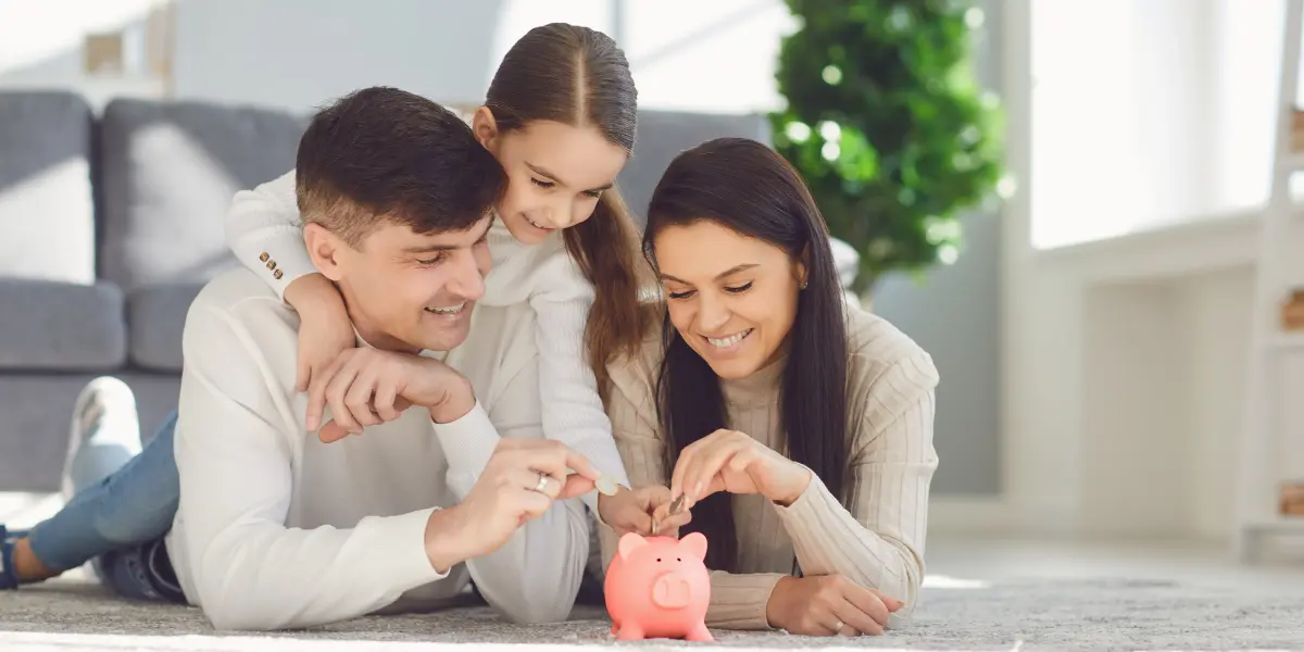 Familj som sparar pengar tillsammans genom att lägga mynt i en spargris, symbol för barnsparande och investeringar inför framtiden.