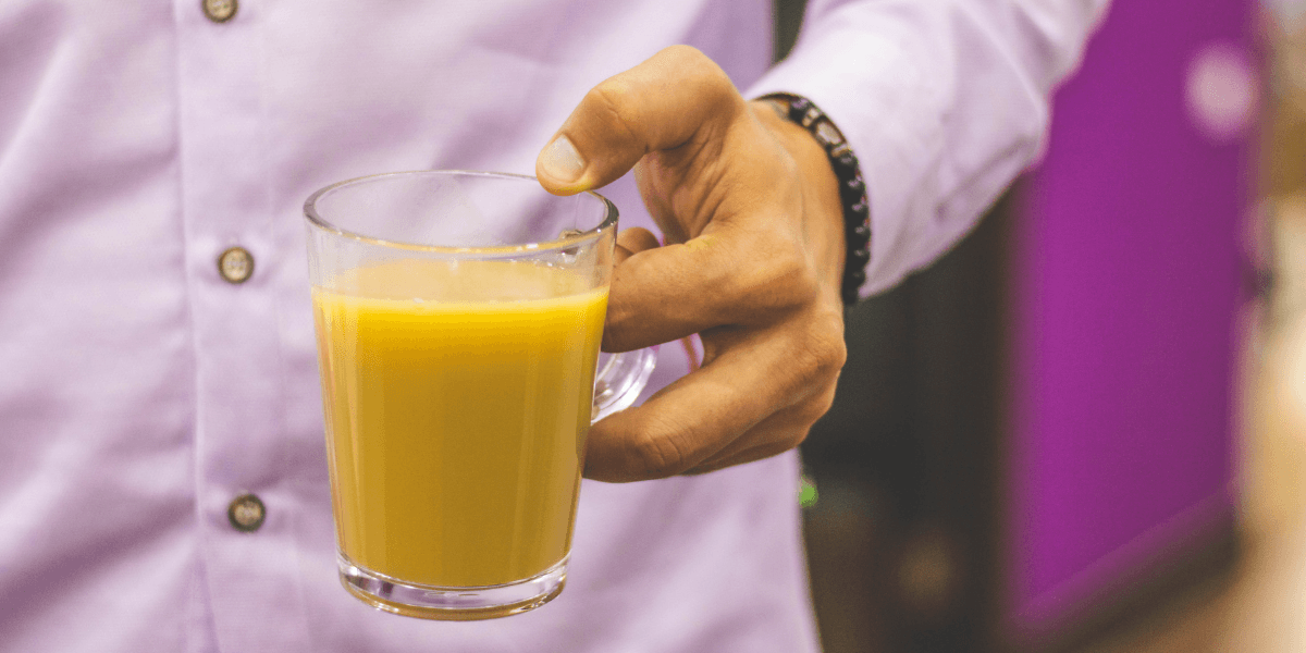 En person i skjorta håller ett glas med apelsinjuice i handen.