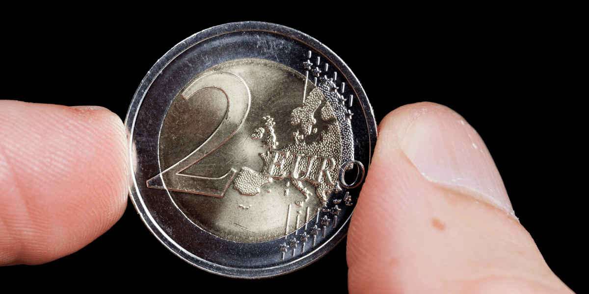 Närbild på ett tvåeurosmynt som hålls mellan två fingrar mot svart bakgrund.