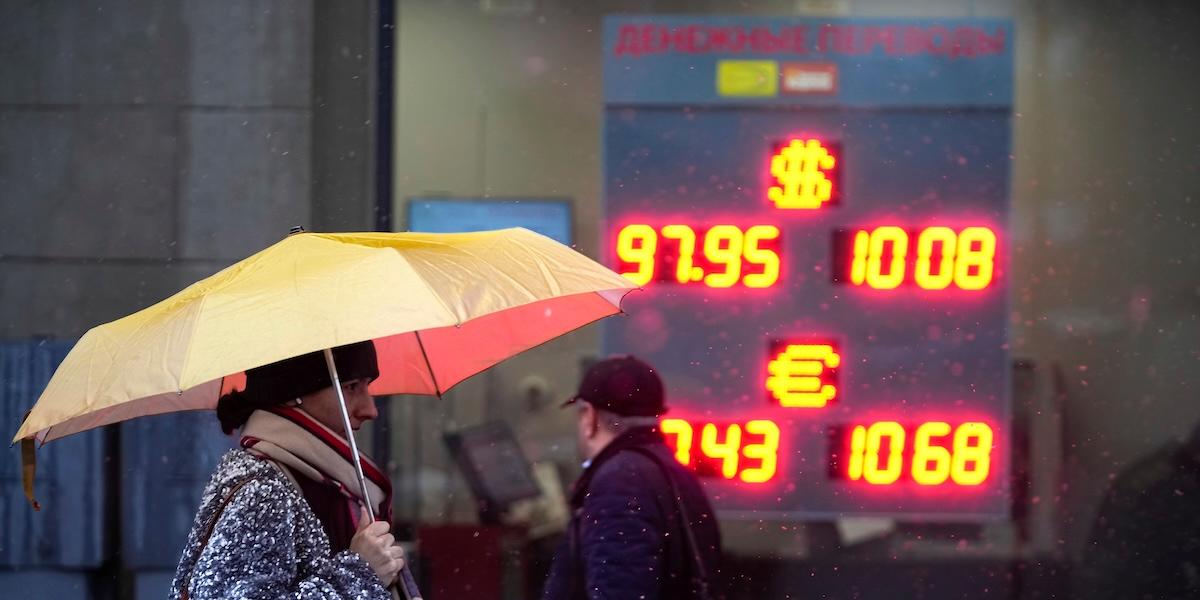 En kvinna med paraply passerar växlingsskylt i Moskva. Inflationen faller, men hushållen påverkas fortfarande av höga räntor och svag rubel.