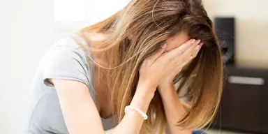 Kvinna med händerna för ansiktet, symbol för hur rikedom och sparande kan påverka relationer och livskvalitet negativt.